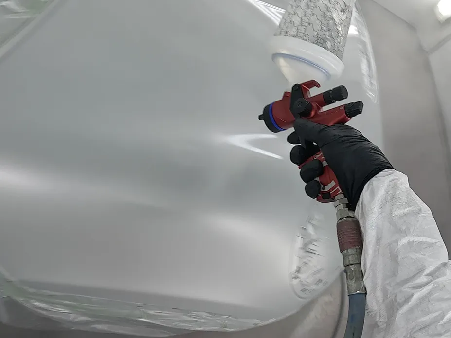 A person using a spray gun to apply paint to a car surface