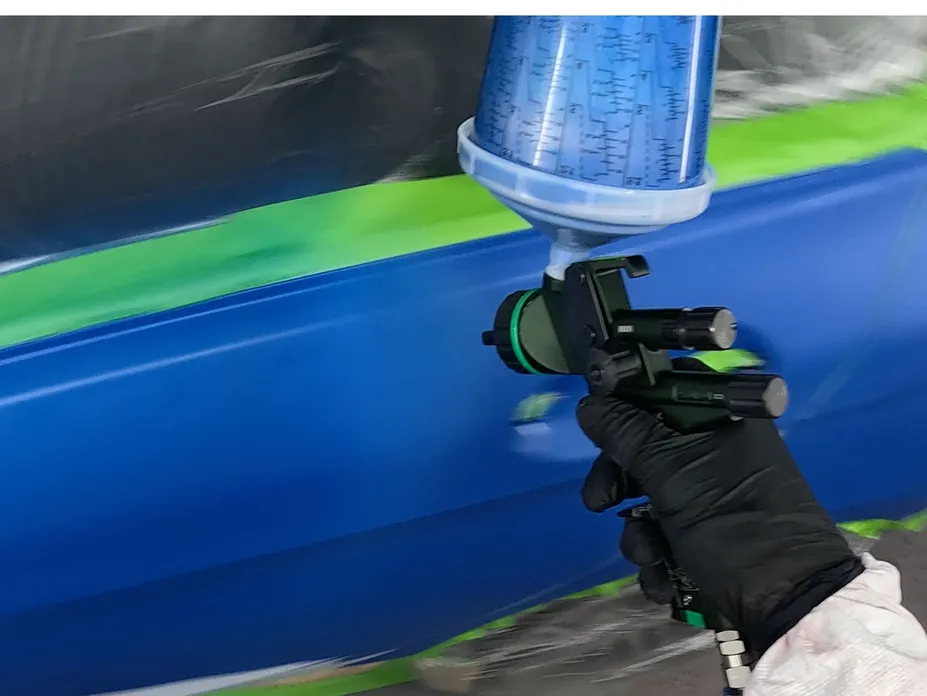 A person spraying blue paint on a car door with a spray gun